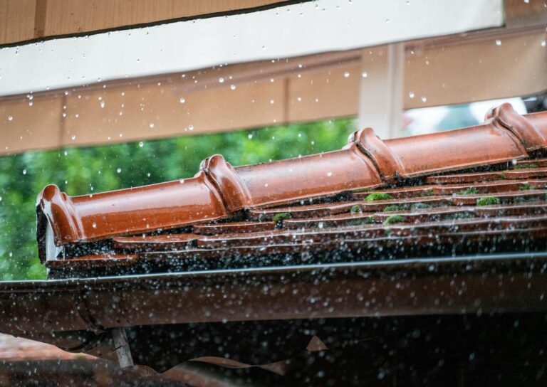 Detailed view of rain droplets cascading off a terracotta roof, capturing the essence of a rainy day.